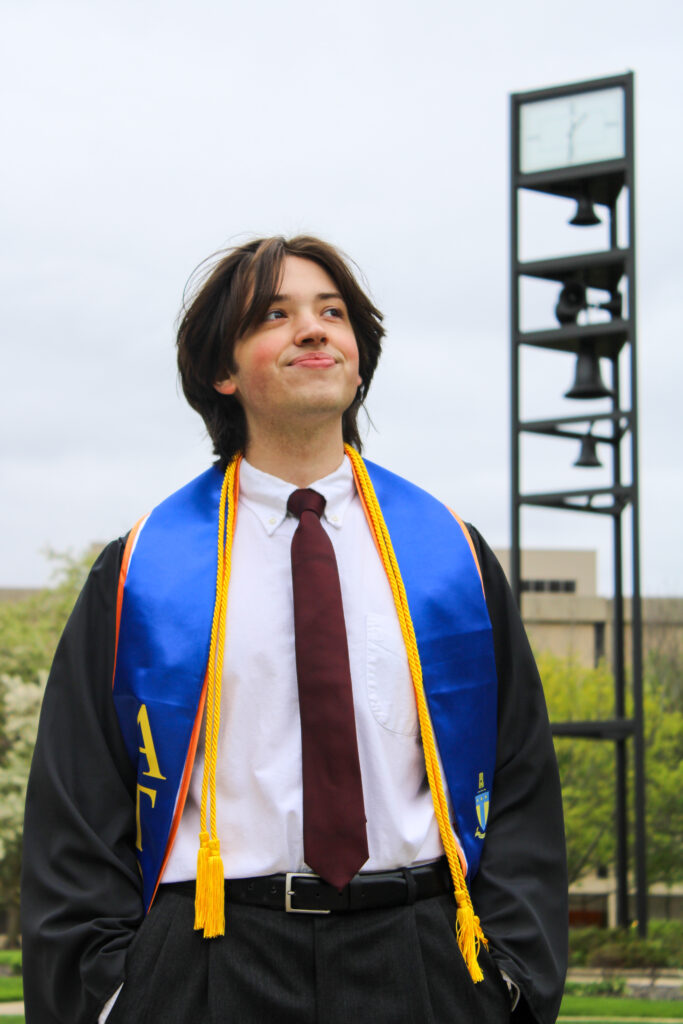 man posing for his senior graduation photos by looking off in the distance. There is a tower slightly behind him and to his right.